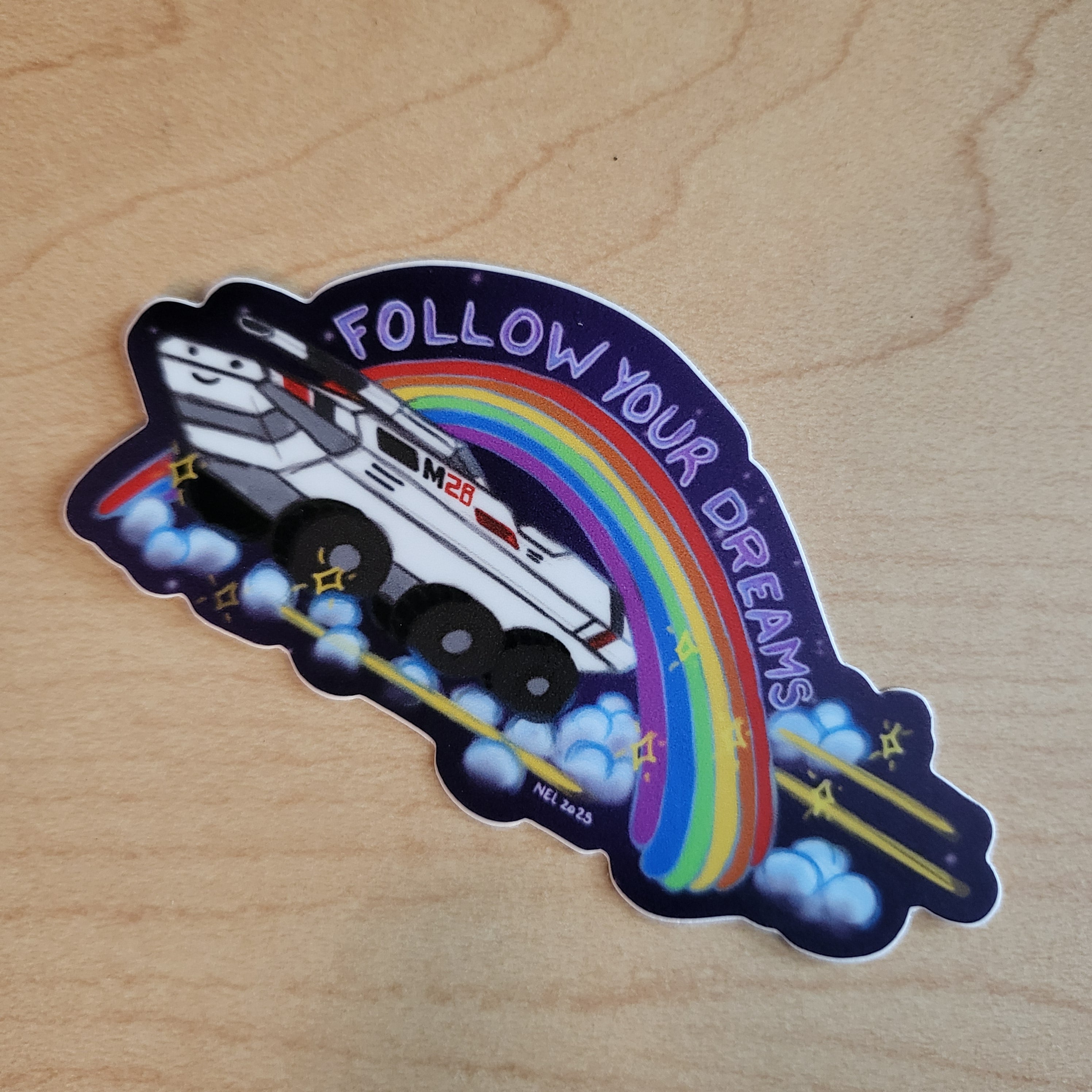 Sticker with a rainbow, space ship, and 'Follow Your Dreams' text on a wooden surface