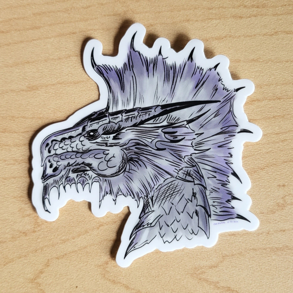 Dragon head sticker with purple accents on a wooden surface