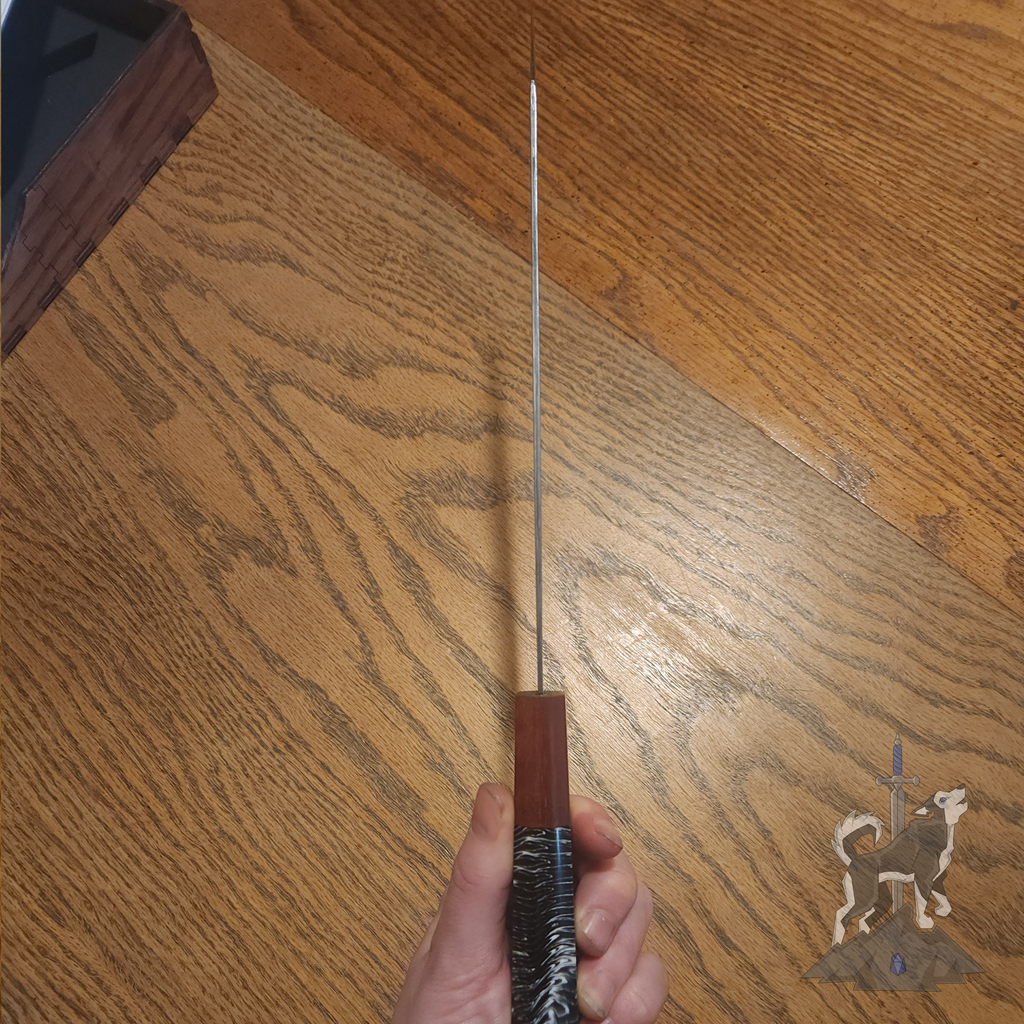 Hand holding a chef knife with Damascus pattern to show the top of the blade over a dark wooden surface.