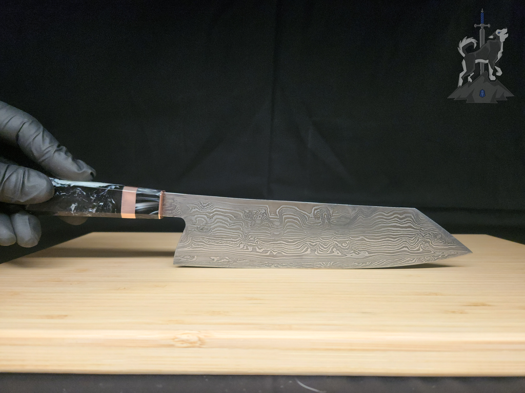Hand holding a Damascus chef's knife on a wooden cutting board with a black background