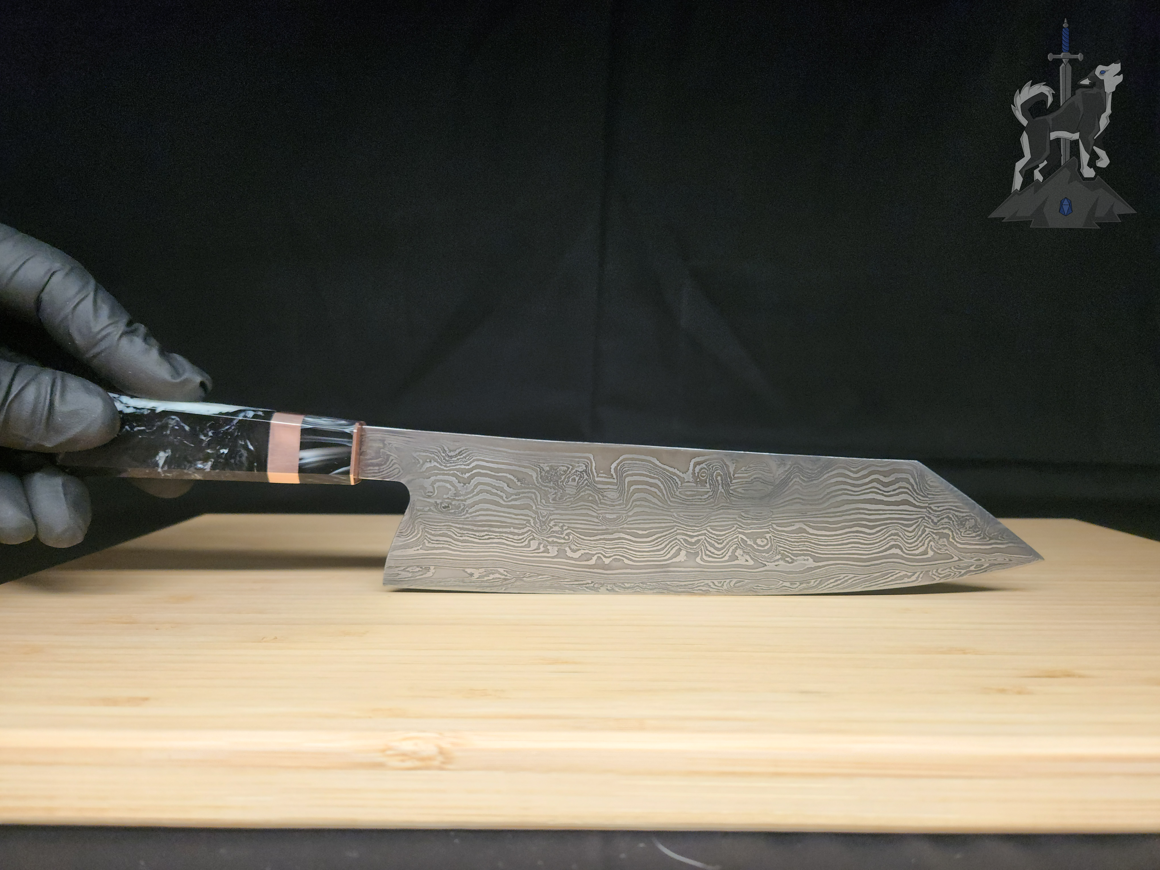 Hand holding a Damascus chef's knife on a wooden cutting board with a black background