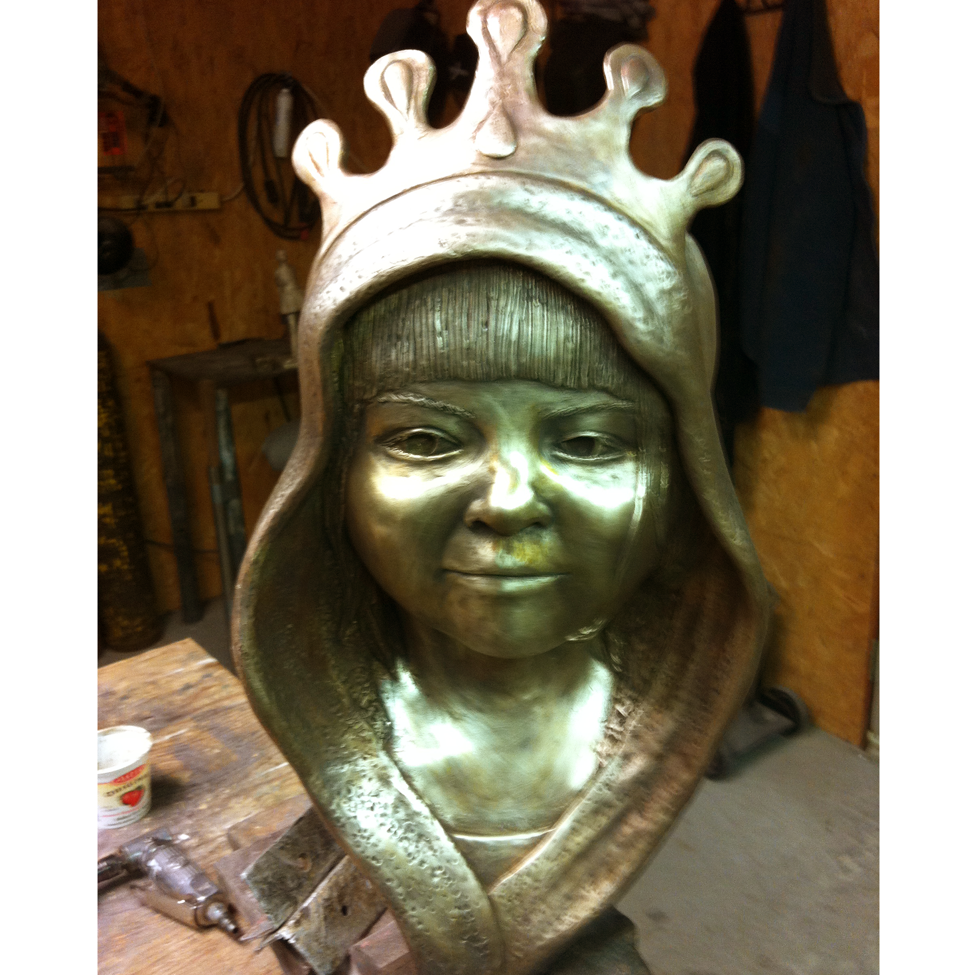 Bronze sculpture recreation of a hooded girl wearing a crown in a workshop setting