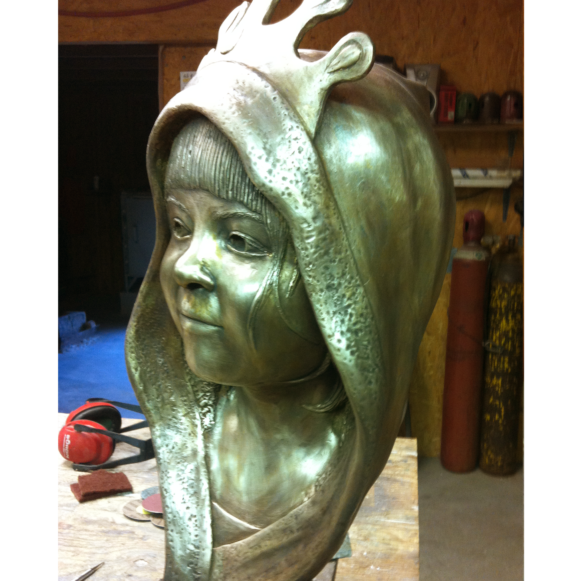 Bronze sculpture recreation of a hooded girl wearing a crown in a workshop setting