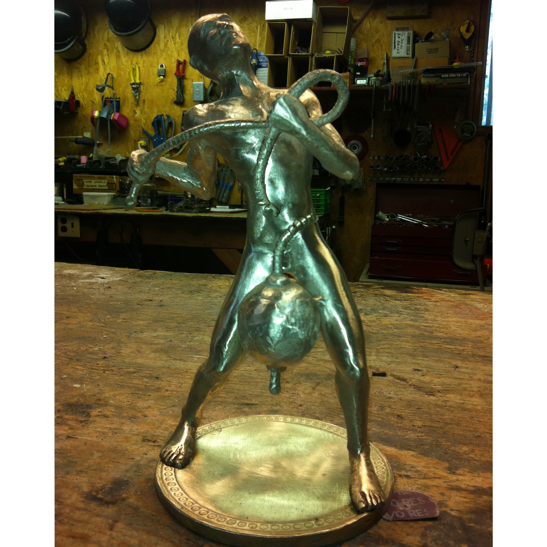 Bronze sculpture recreation of a man holding a ball on a thick rope in a workshop setting