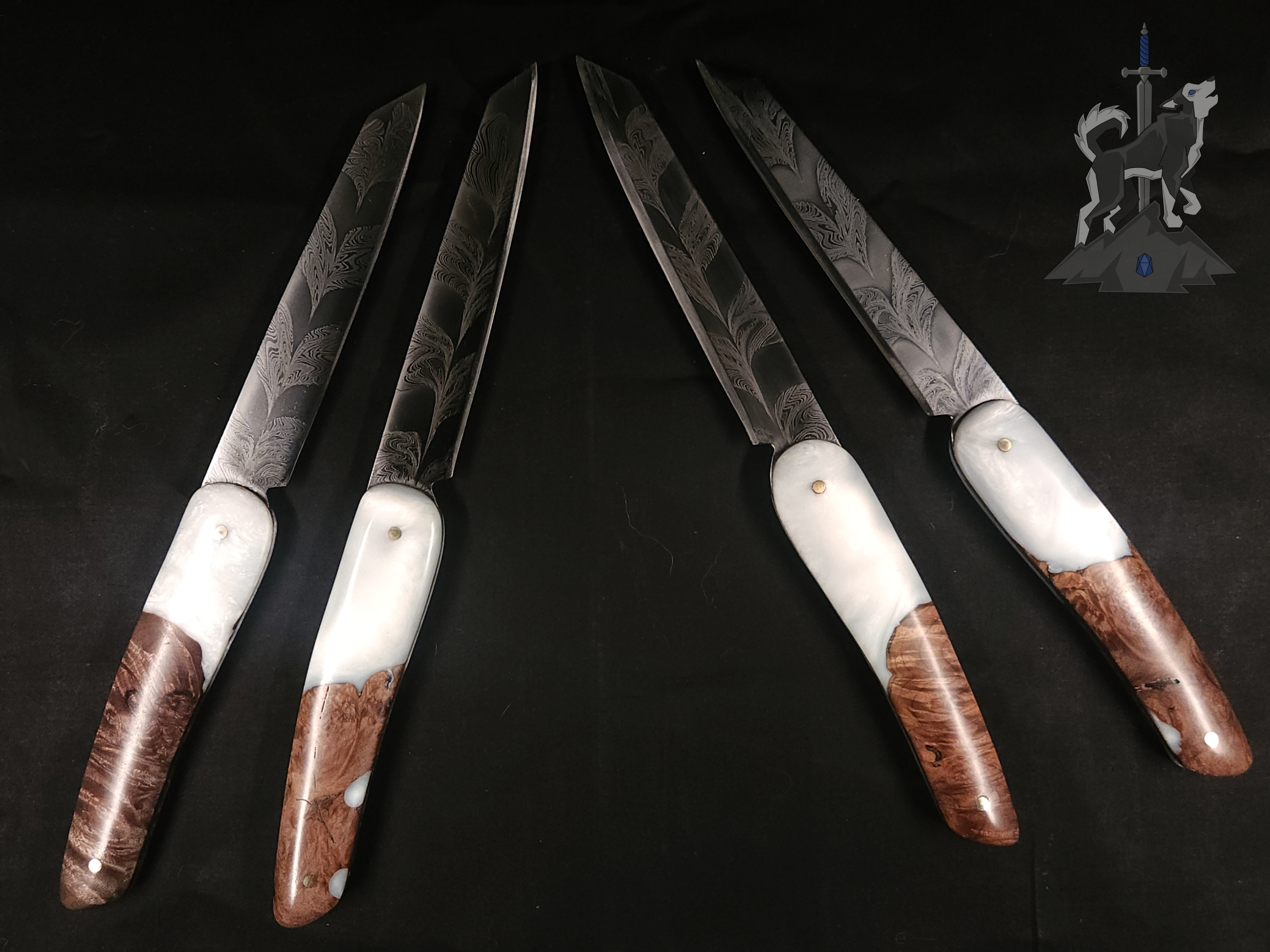 Four feather patterned Damascus steak knives with white and wooden handles on a dark background