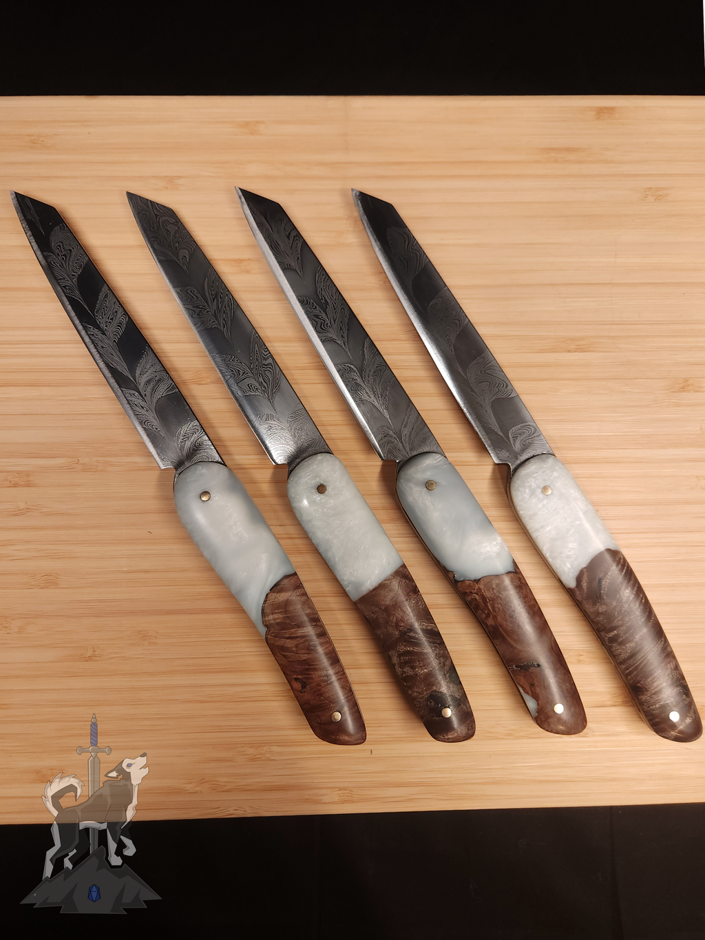 Four feather patterned Damascus steak knives with white and wooden handles on a wooden cutting board.