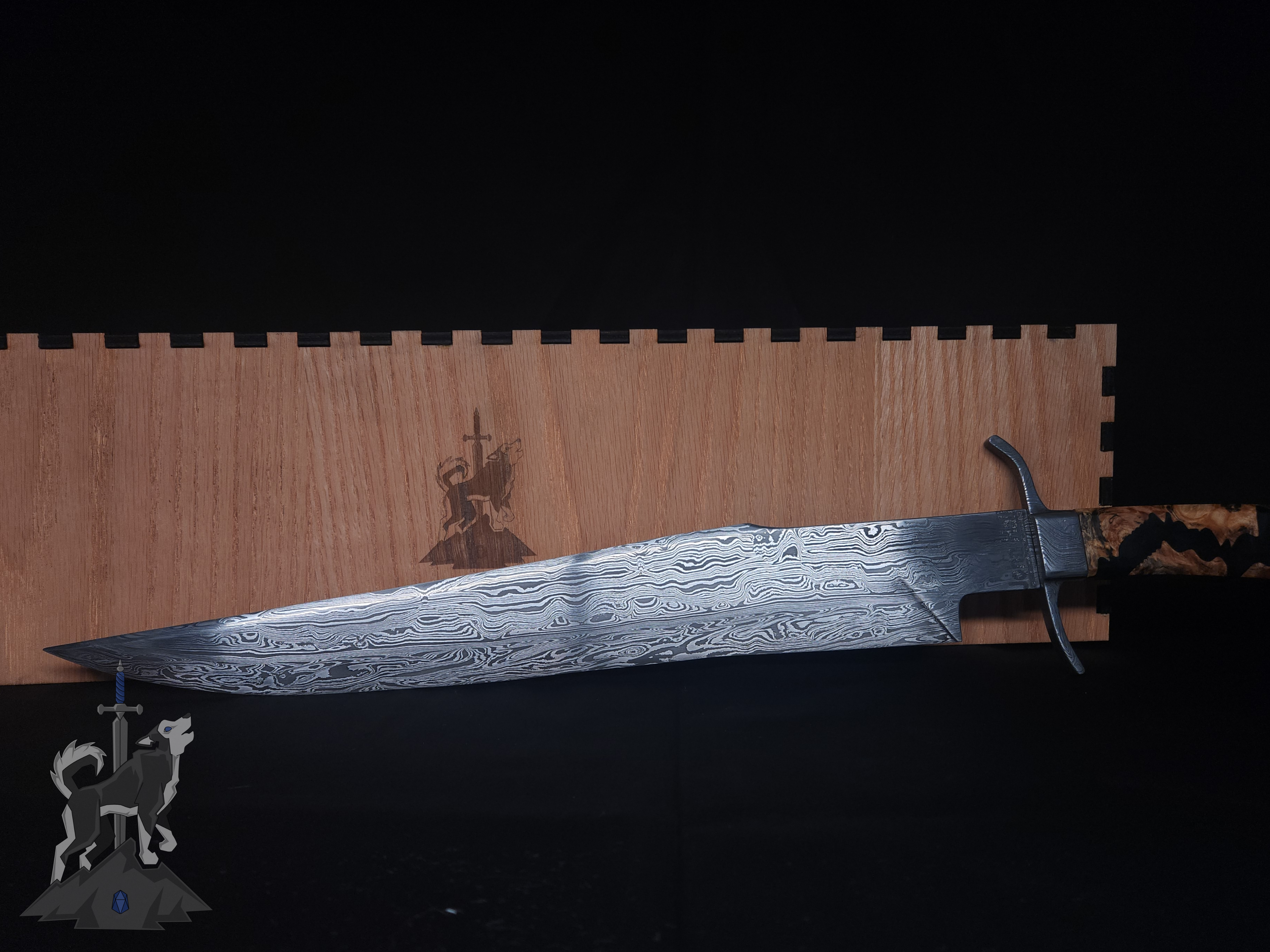 A custom Damascus takedown bowie in front of the storage box on a dark background.