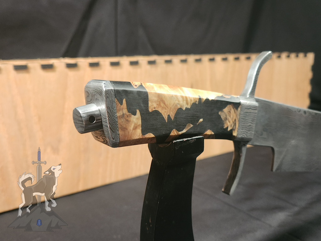 Detailed shot of the pommel and nut on the handle of the custom Damascus takedown bowie with the storage box behind it slightly out of focus on a dark background.