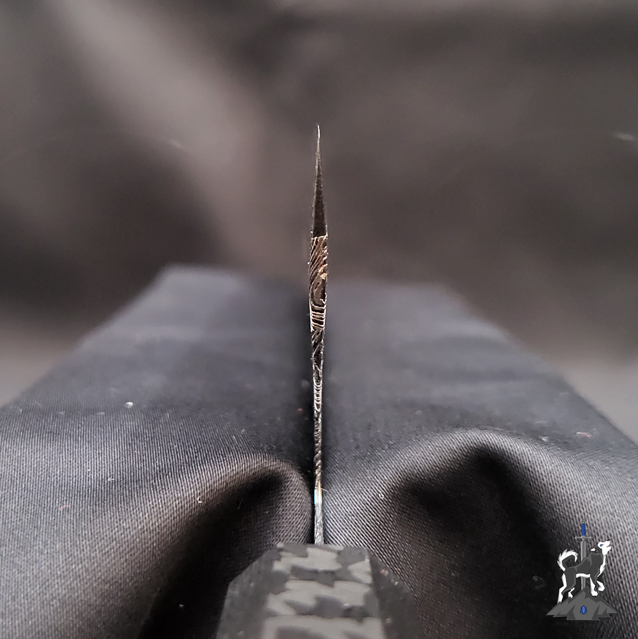 Close-up of a Damascus chef knife choil with a blurred black background.