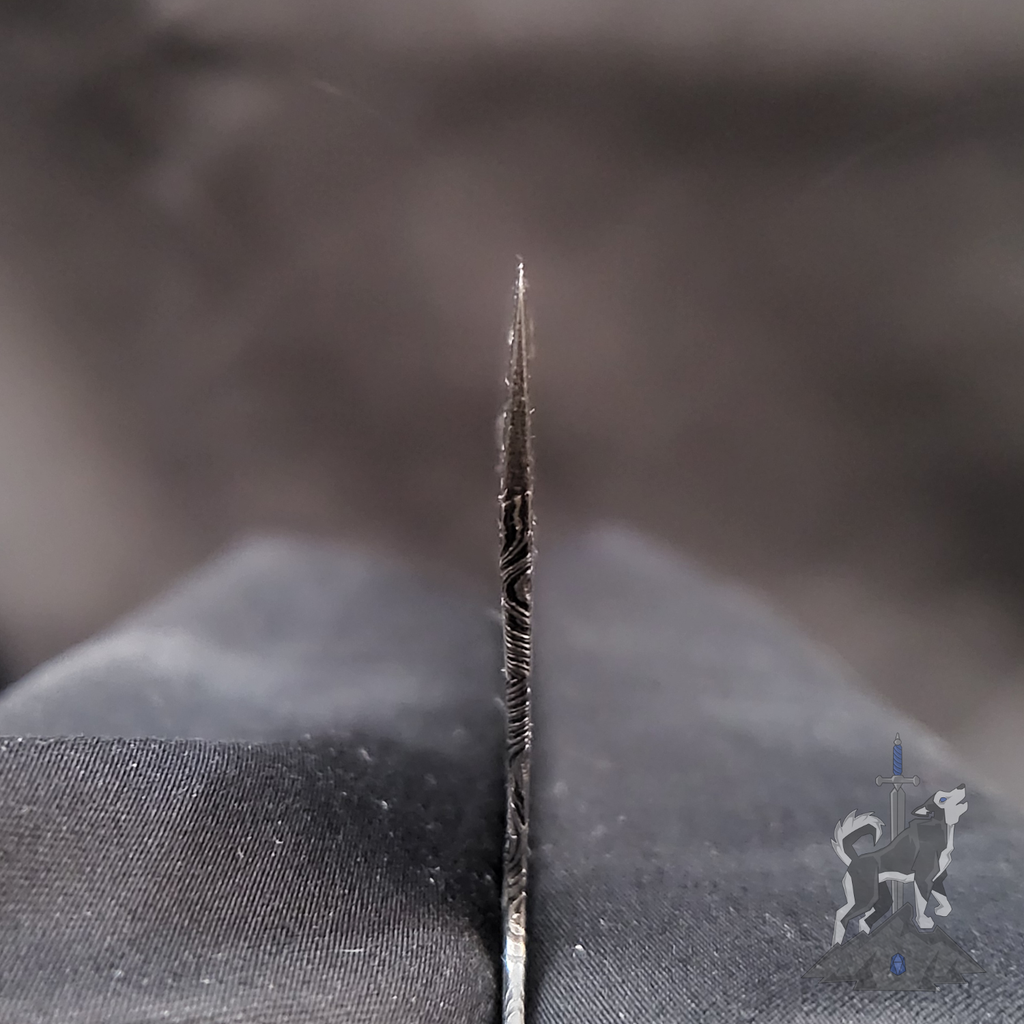Close-up of a Damascus chef knife choil with a blurred black background.