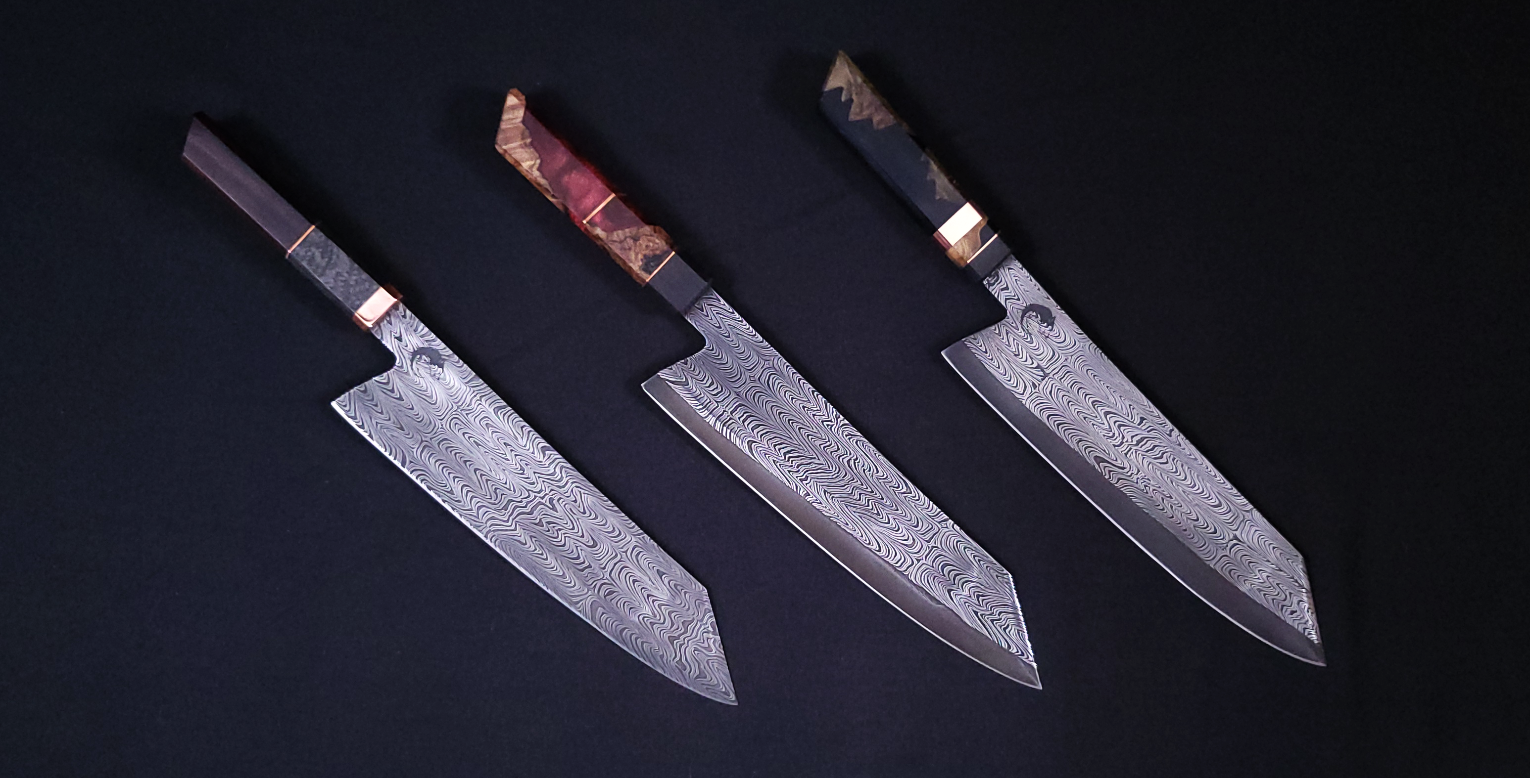 Three Damascus steel kitchen knives on a black surface