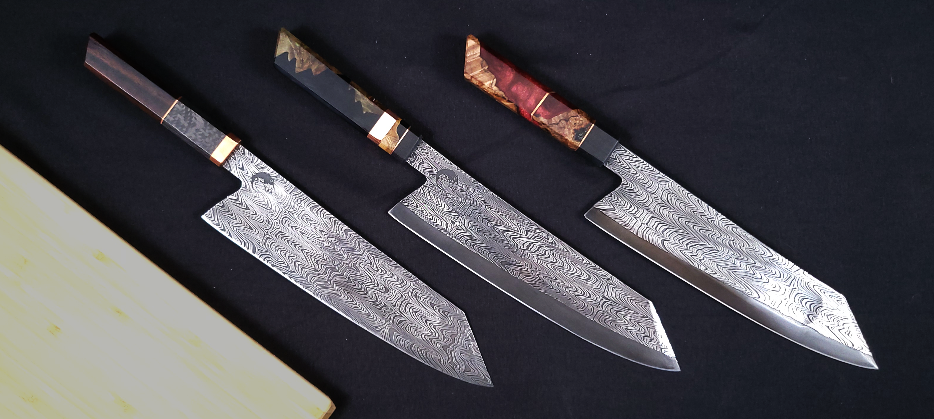 Three Damascus steel knives with wooden handles on a dark surface